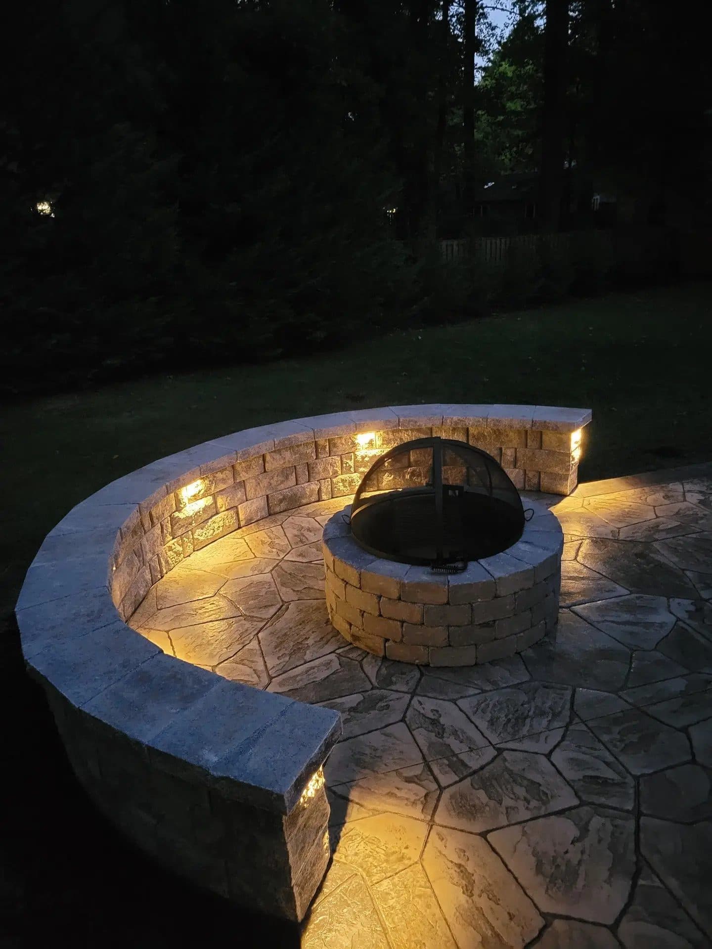Finished circular stamped concrete patio with stone seating wall and fire pit, evening