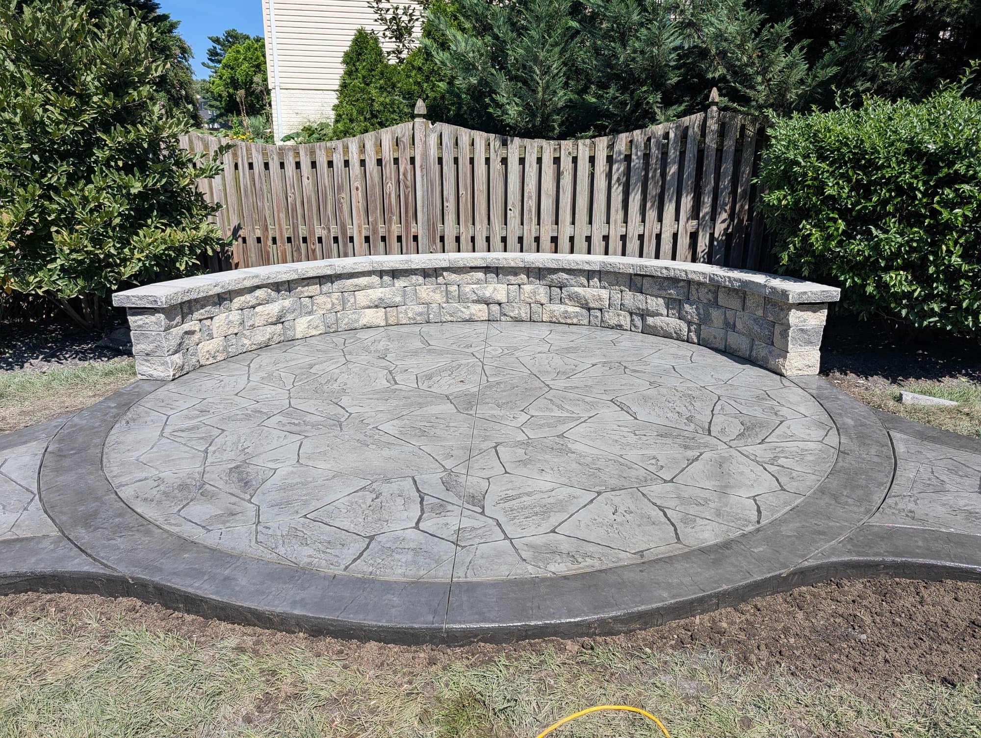 Circular stamped concrete patio in a light gray flagstone pattern with a curved tan segmental-block seating wall