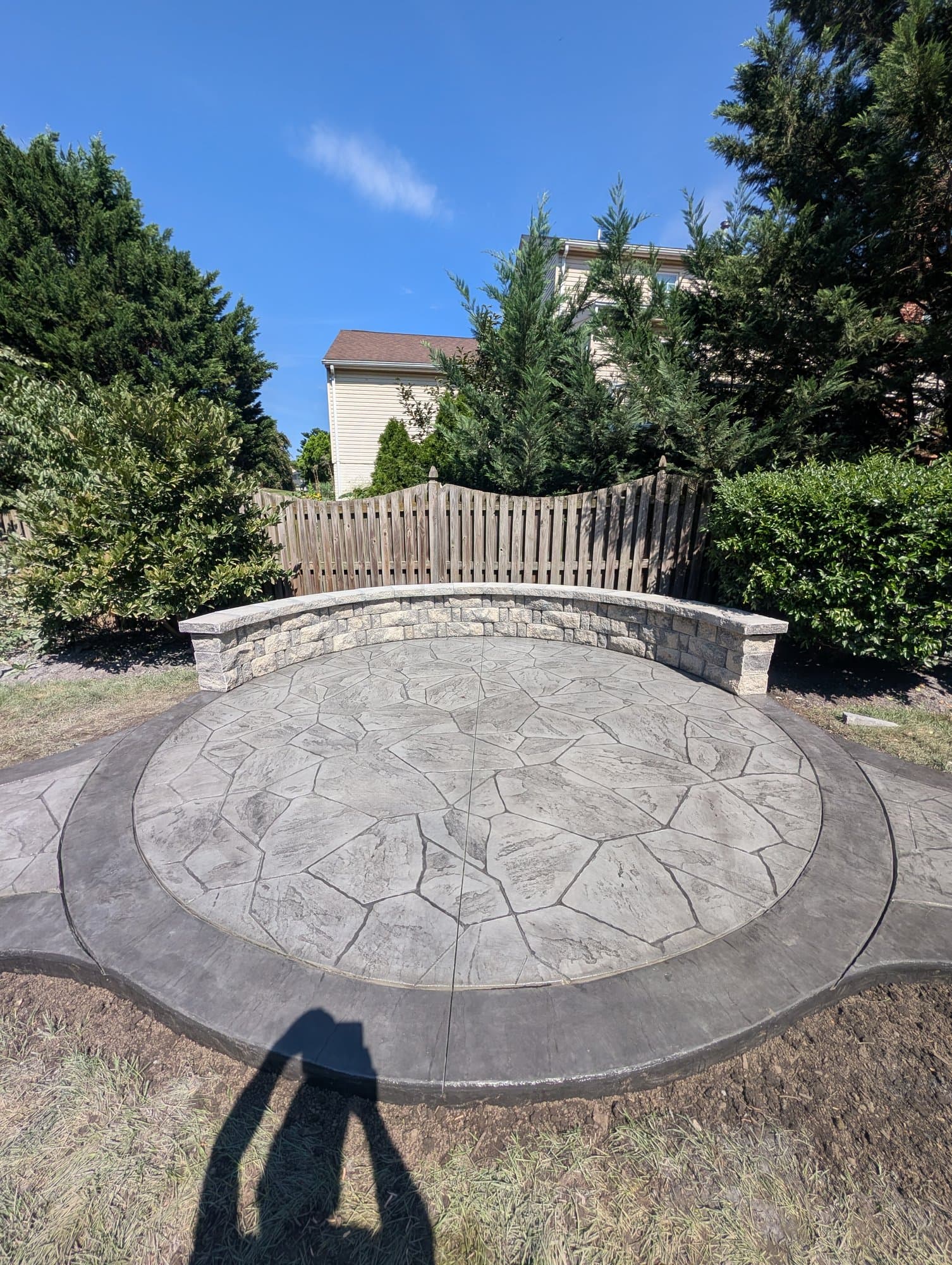 Circular stamped concrete patio with a curved tan segmental-block seating wall, wide view