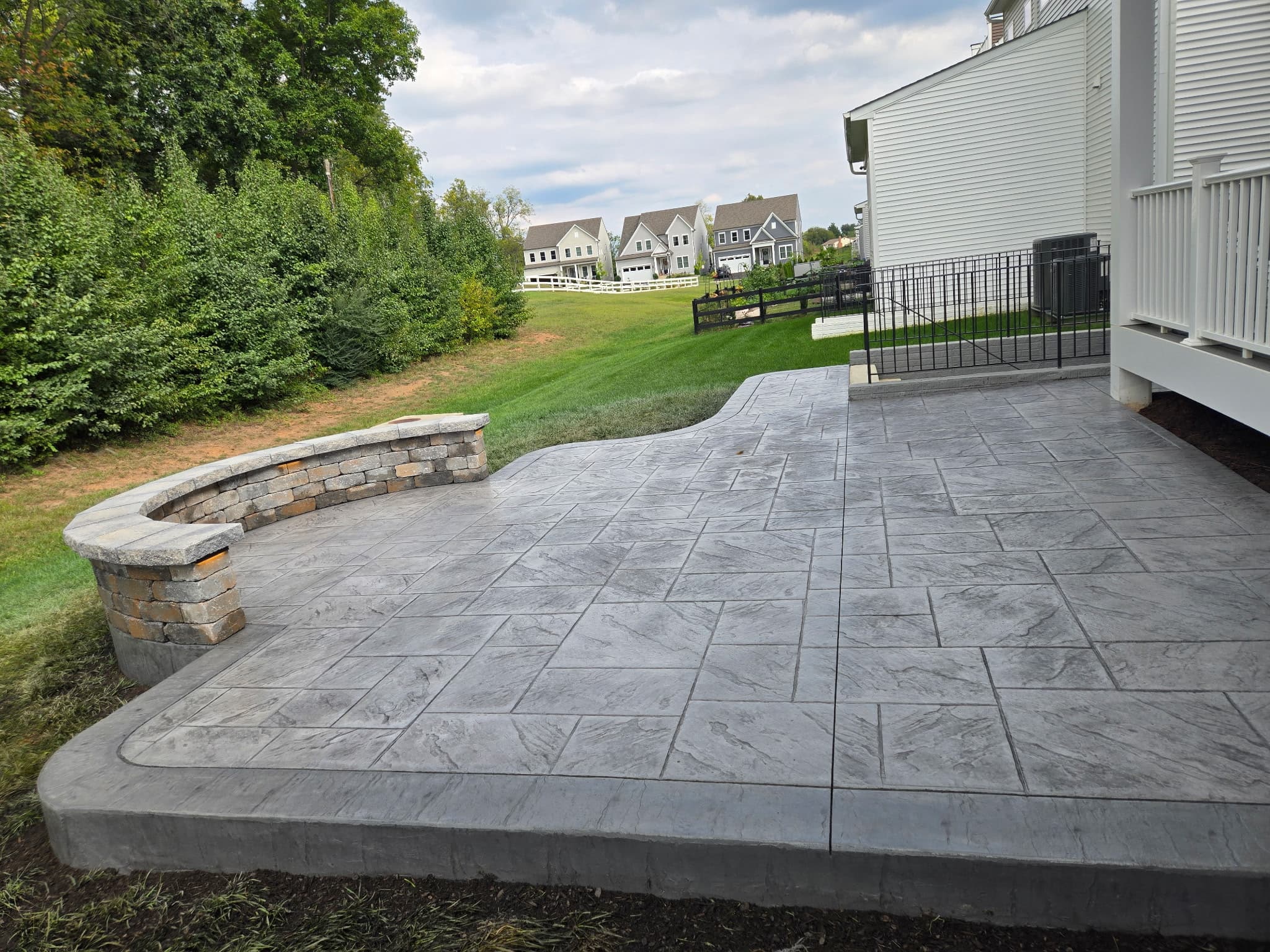 Finished gray flagstone-pattern stamped concrete patio in Aldie, VA, with a curved stone seating wall, alternate angle